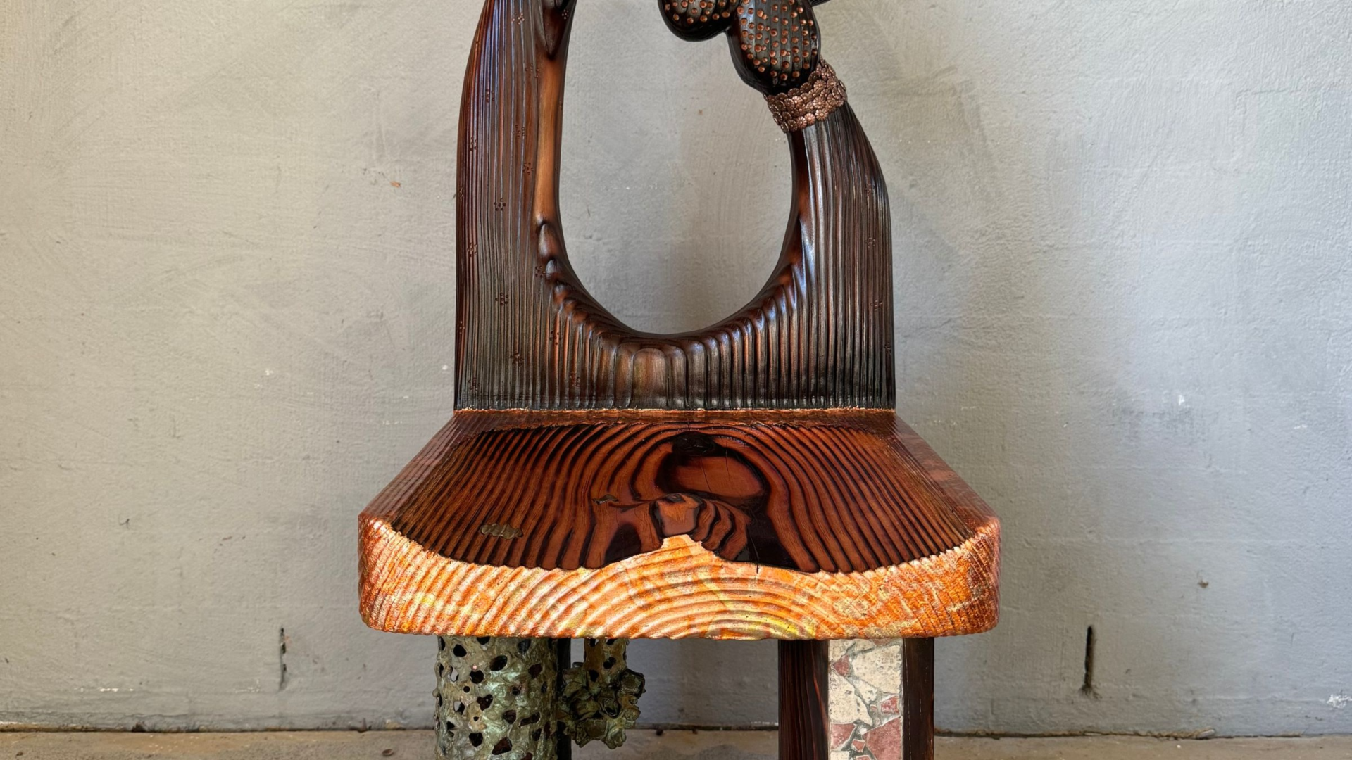 Detail photo of hand carved wooden chair adorned in mixed materials.